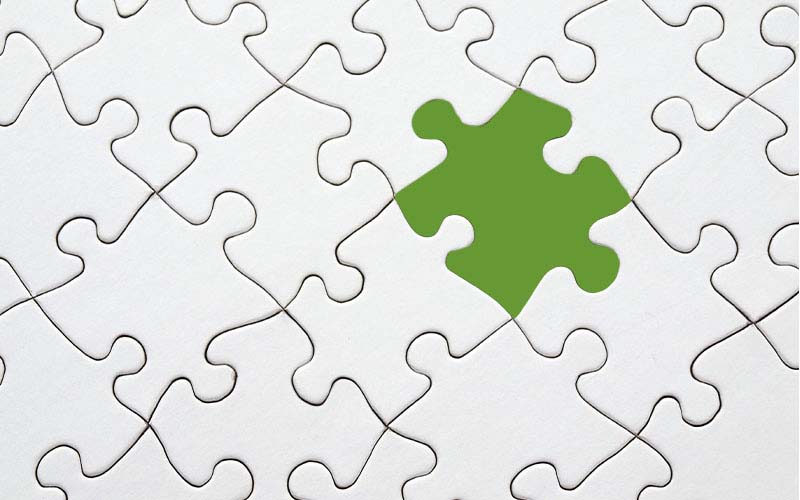 A puzzle with all white pieces and one green piece 