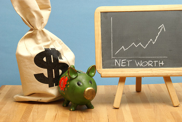 piggy bank with bag of money and board showing a net worth graph trending upward