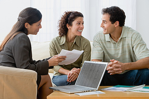 Three people gathered around a laptop and paperwork while talking.