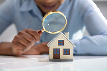 A person holding a magnifying glass to a miniature house