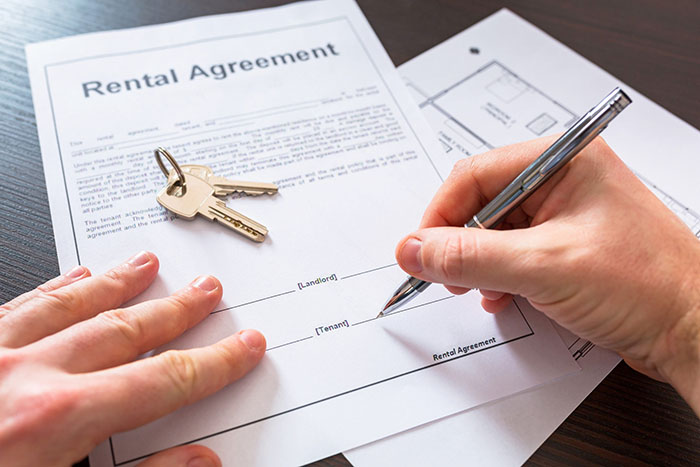 A person signing a rental agreement with keys on the paper