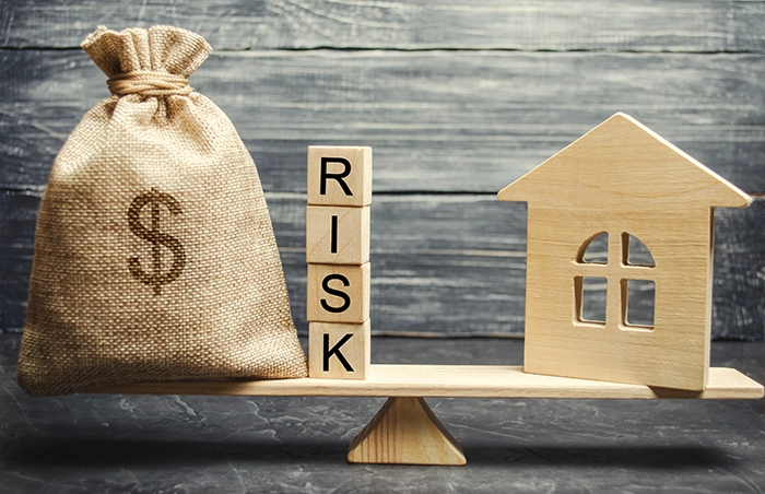 seesaw with a house on one end and a bag of money on the other with the word risk in the middle showing the risk and reward from real estate investing